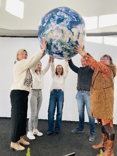 Vier weibliche und eine männliche Person stehen im Halbkreis auf einer Bühne und halten gemeinsam ein aufblasbares Modell des Planeten Erde in die Höhe.